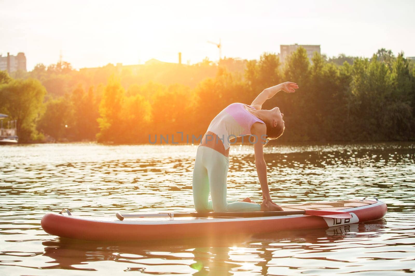 Young woman doing yoga on sup board with paddle. Yoga pose, side view - concept of harmony with the nature. by nazarovsergey