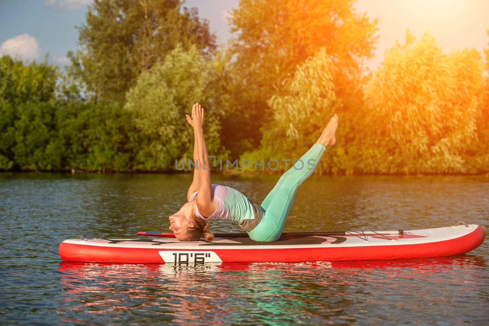 Young woman doing yoga on sup board with paddle. Yoga pose, side view - concept of harmony with the nature. by nazarovsergey
