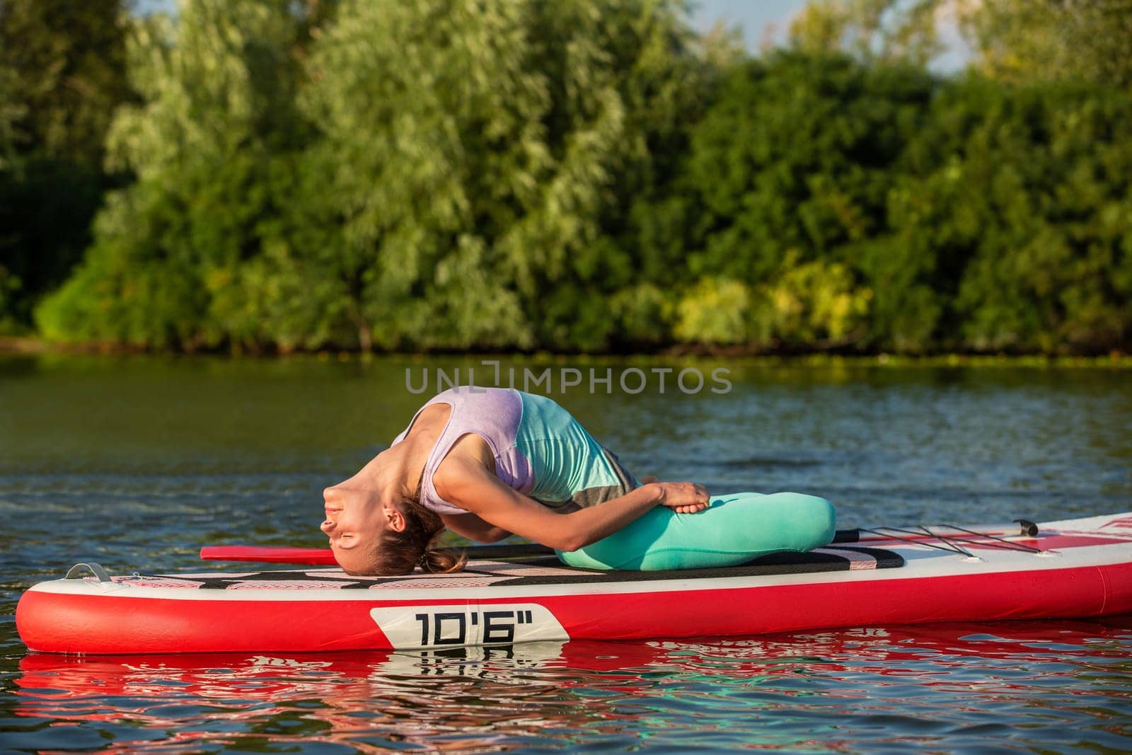Woman practicing yoga on the paddle board in the morning by nazarovsergey