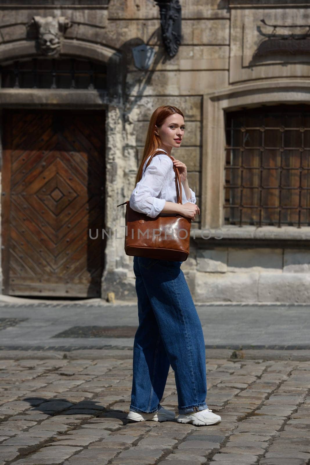 photo of a woman with a leather bag. the girl is dressed in jeans, a white blouse and sneakers