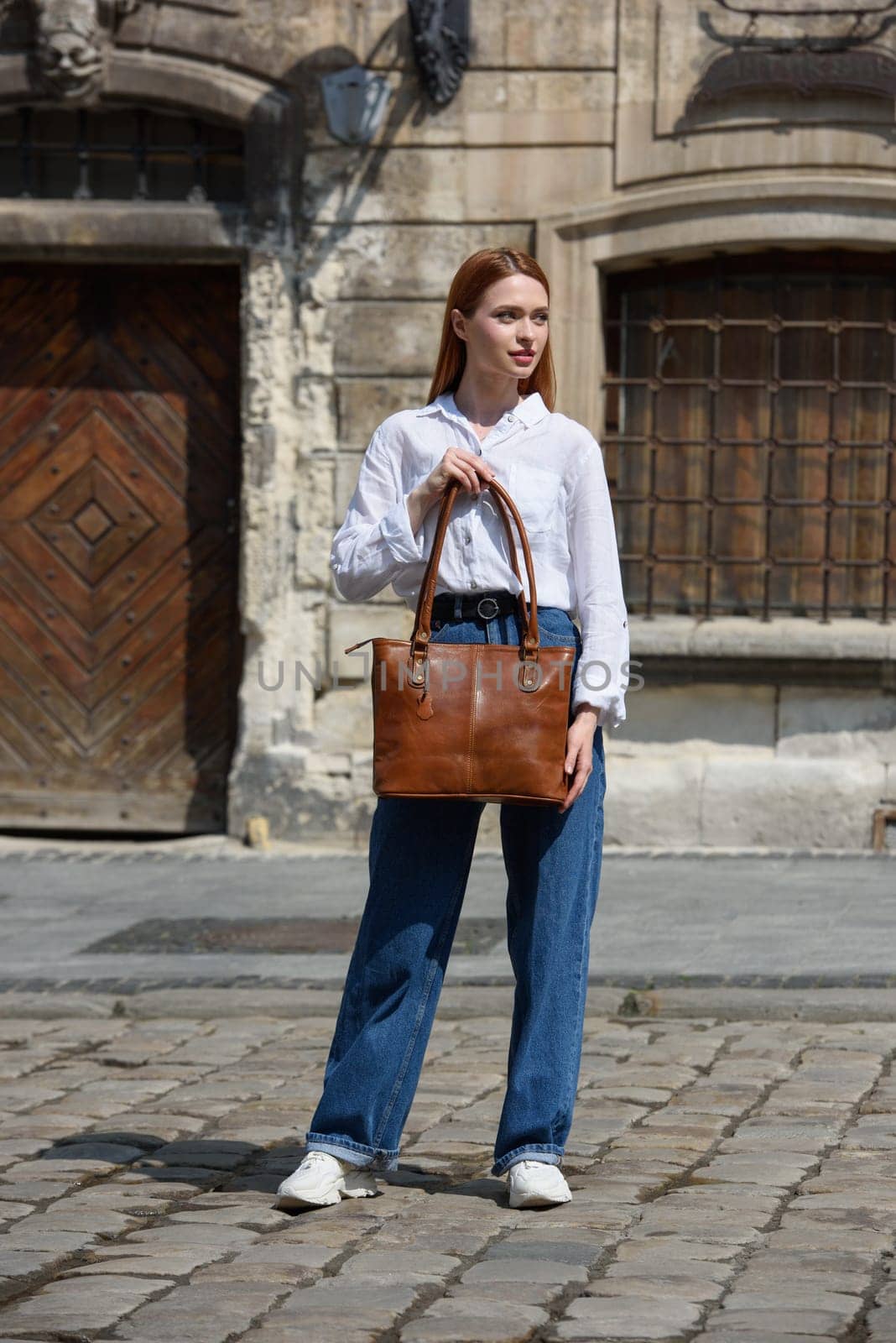 photo of a woman with a leather bag. the girl is dressed in jeans, a white blouse and sneakers