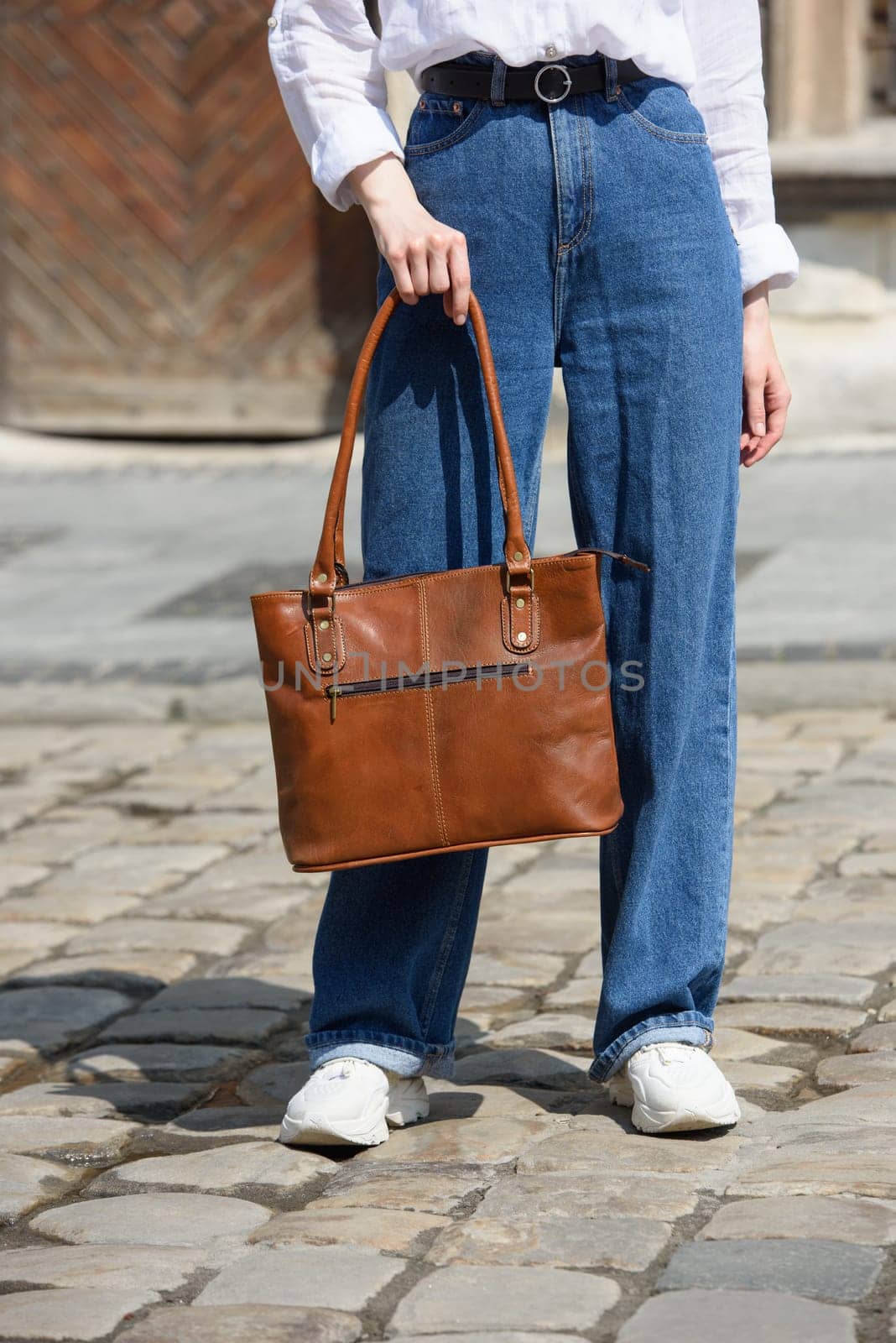 photo of a woman with a leather bag. the girl is dressed in jeans, a white blouse and sneakers