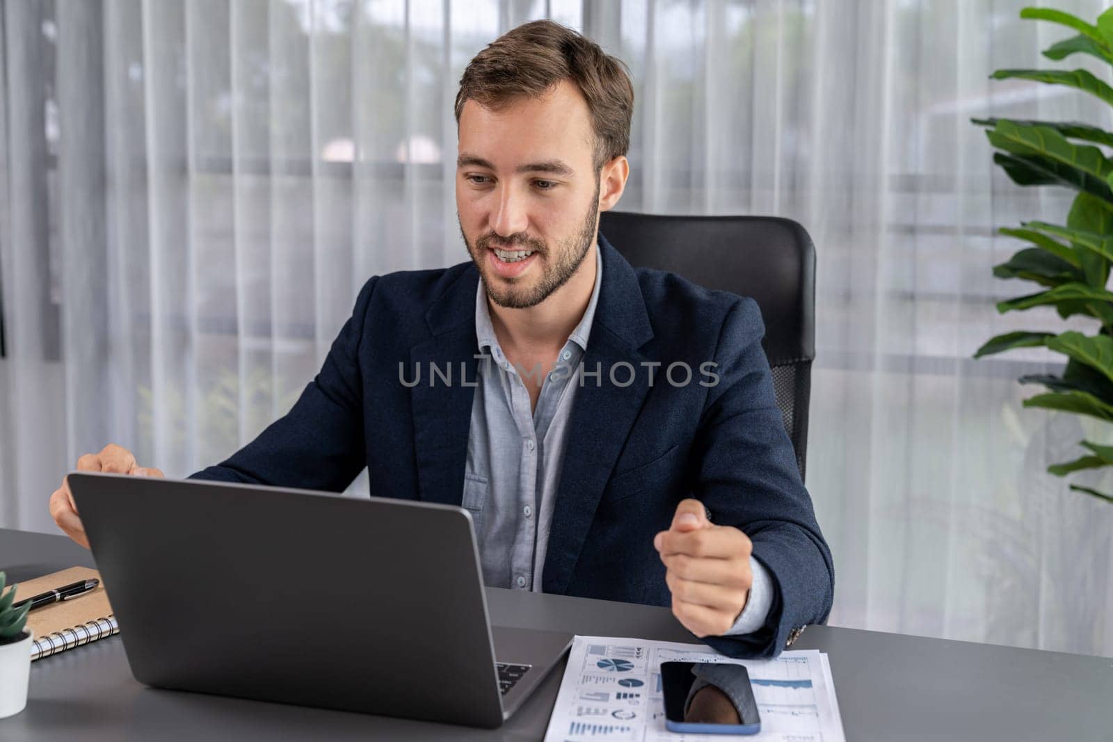 Businessman holds virtual office meeting from office desk, discussing with online video conference using webinar application on laptop for distant communication with remote workers. Entity
