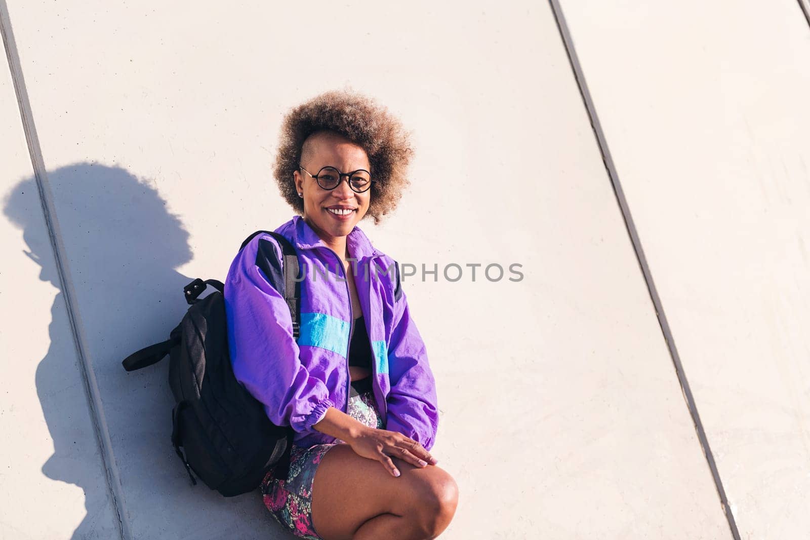 portrait of a smiling african american young woman in sports clothes leaning on an urban wall, concept of active lifestyle and urban sport, copy space for text