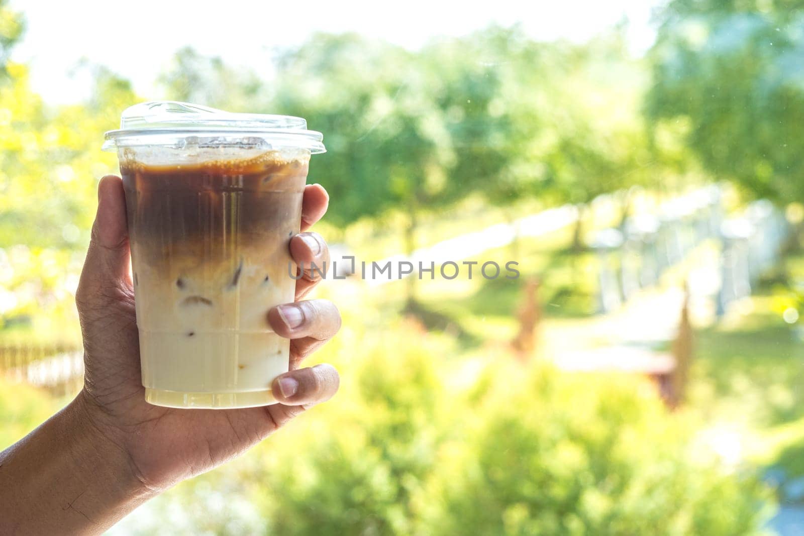 Hand Holding Iced Latte Coffee on blur green nature background