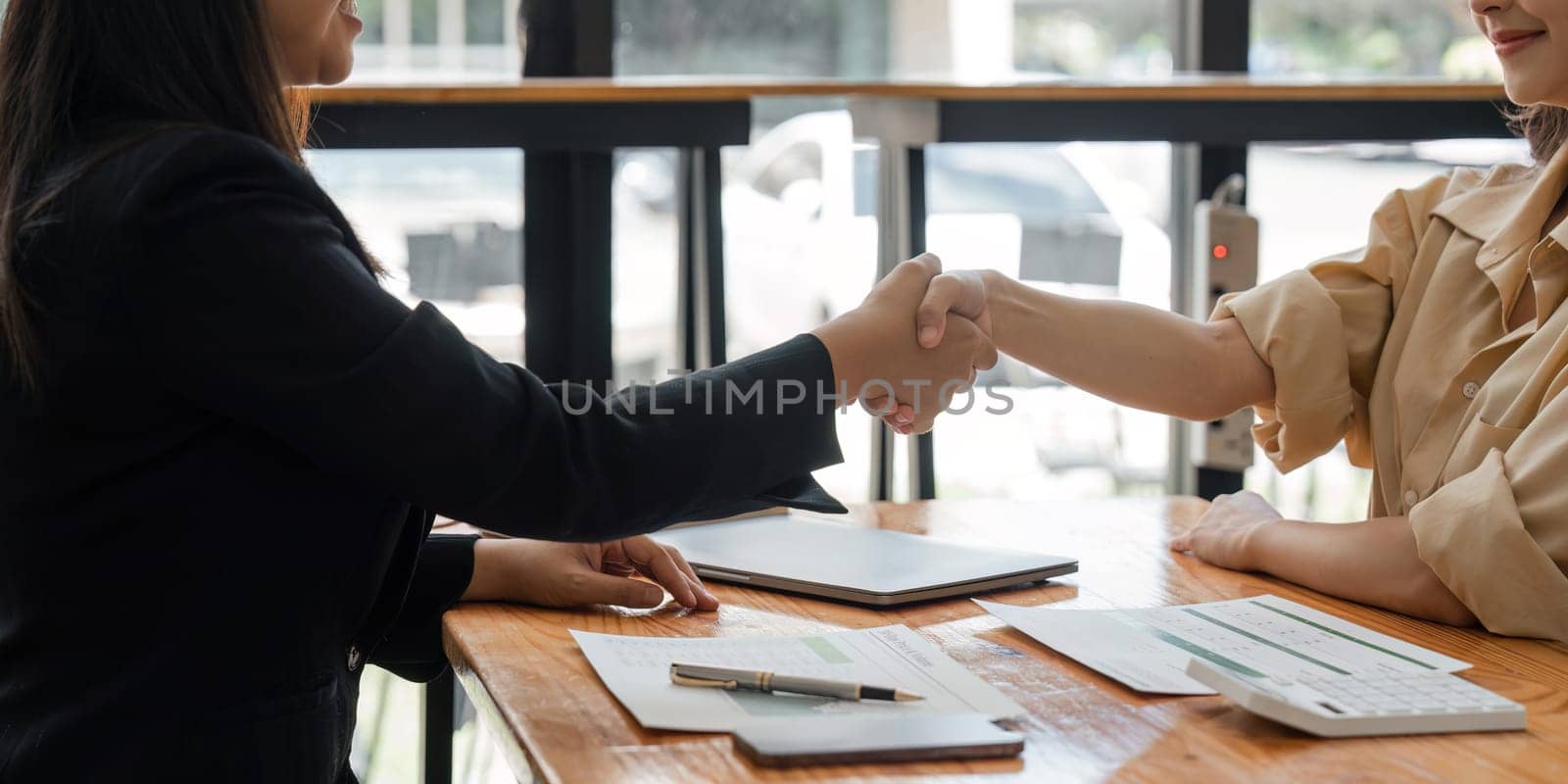 businesspeople shake hand after their partnerships in conference room and finalized pile of papers of financial report and data analysis on meeting table.