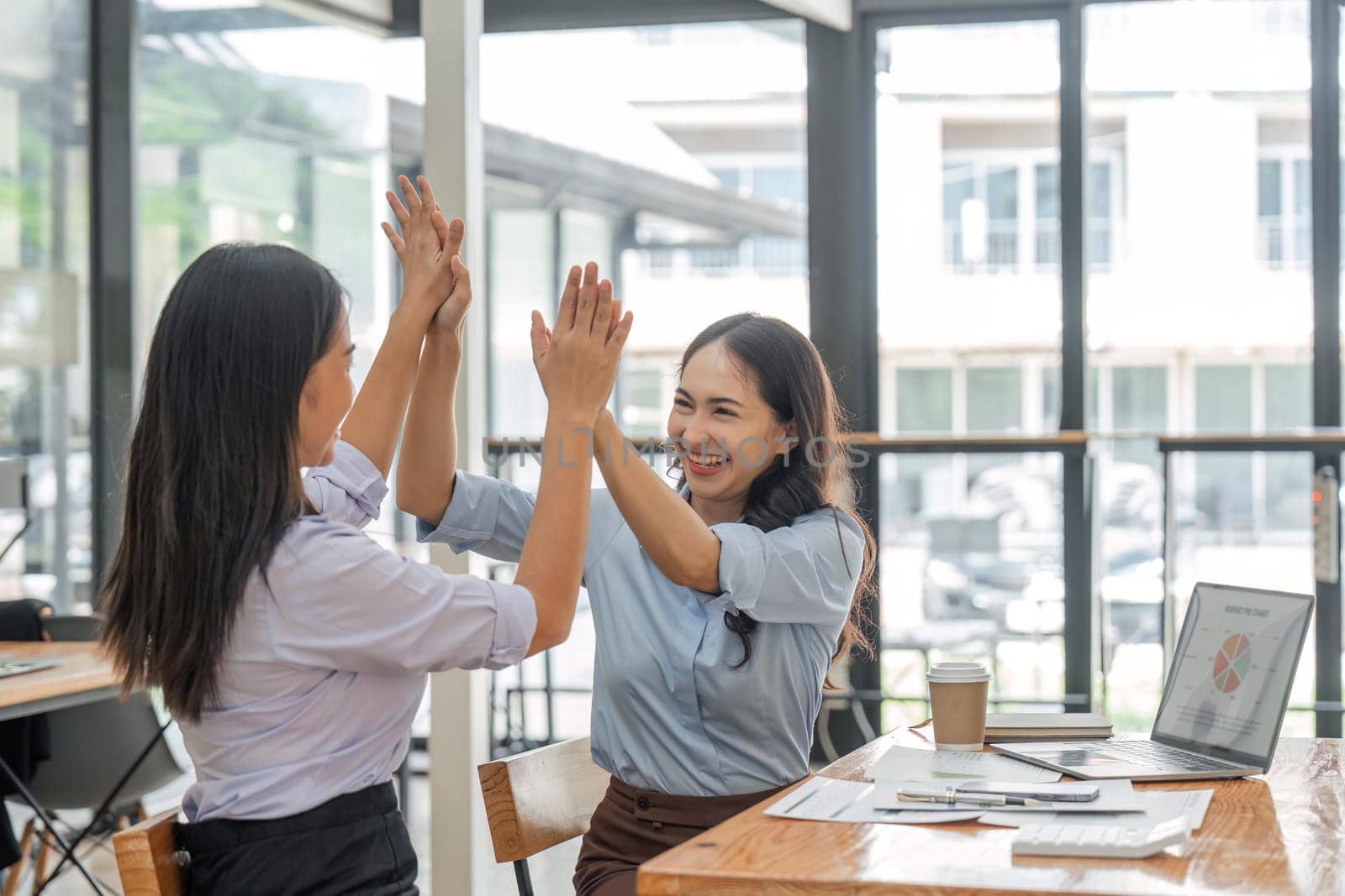 Excited asian business team giving high five at office meeting motivated by victory, achievement or good work result.