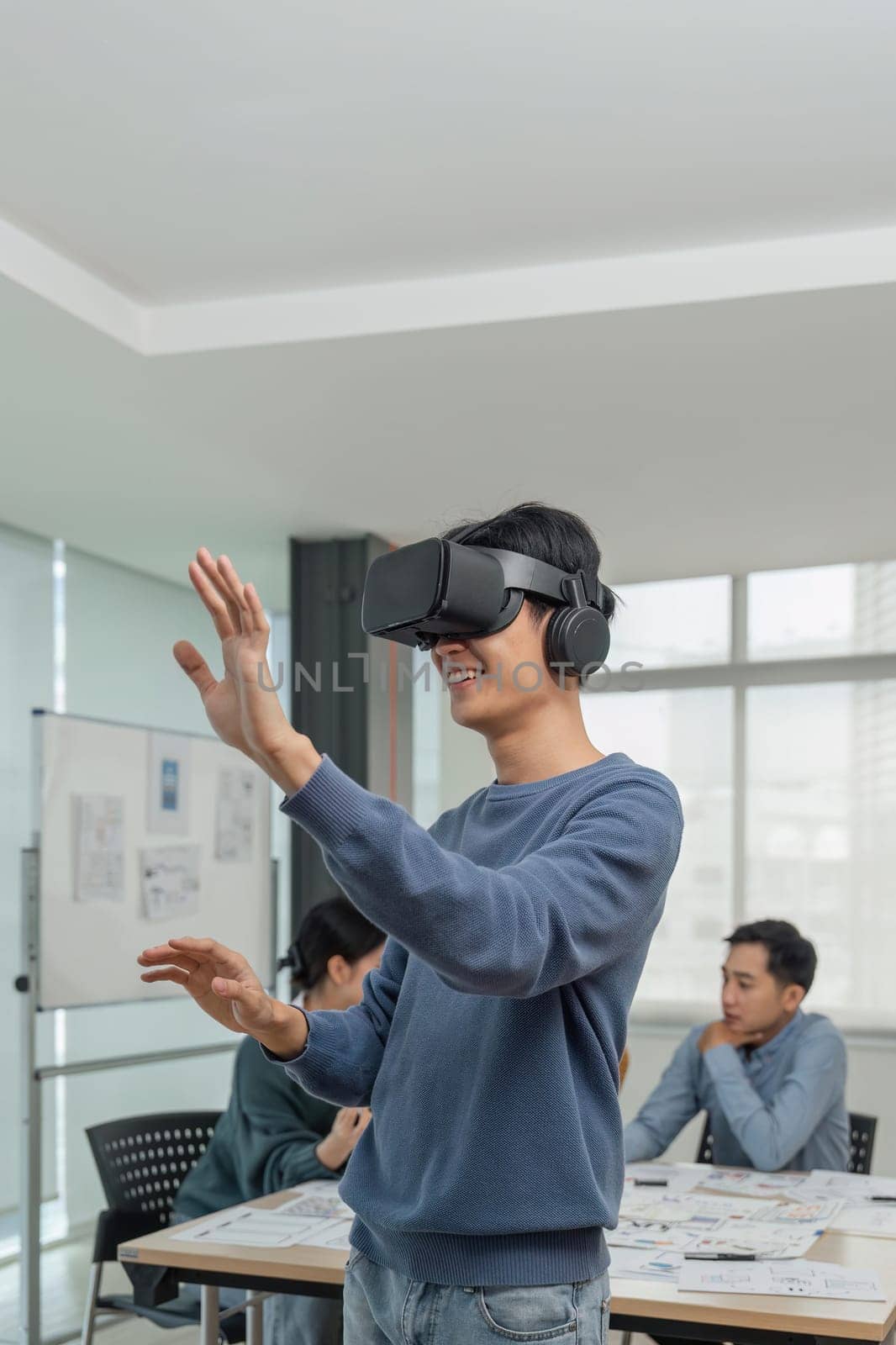 A cheerful and excited young Asian male developer tested a new VR game on a VR headset in the meeting with team. Virtual reality.