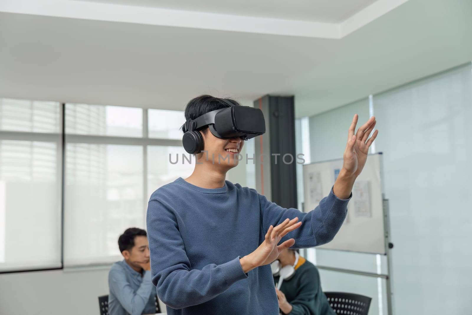A cheerful and excited young Asian male developer tested a new VR game on a VR headset in the meeting with team. Virtual reality by nateemee
