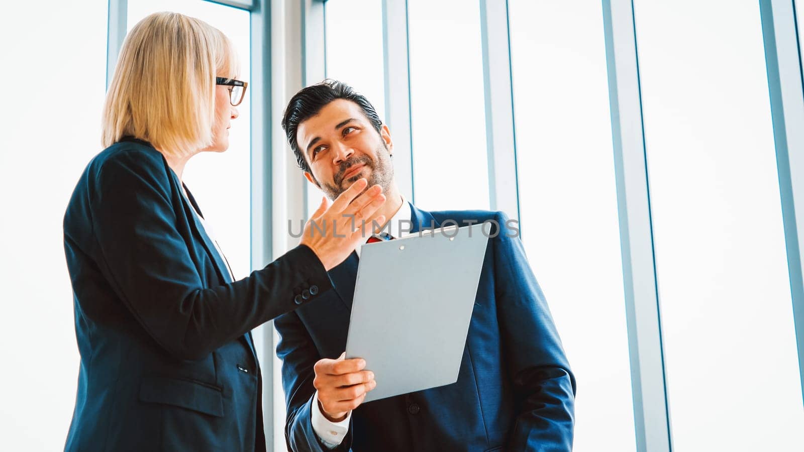 Two business people talk project strategy at office meeting room. Businessman discuss project planning with colleague at modern workplace while having conversation and advice on financial report. Jivy