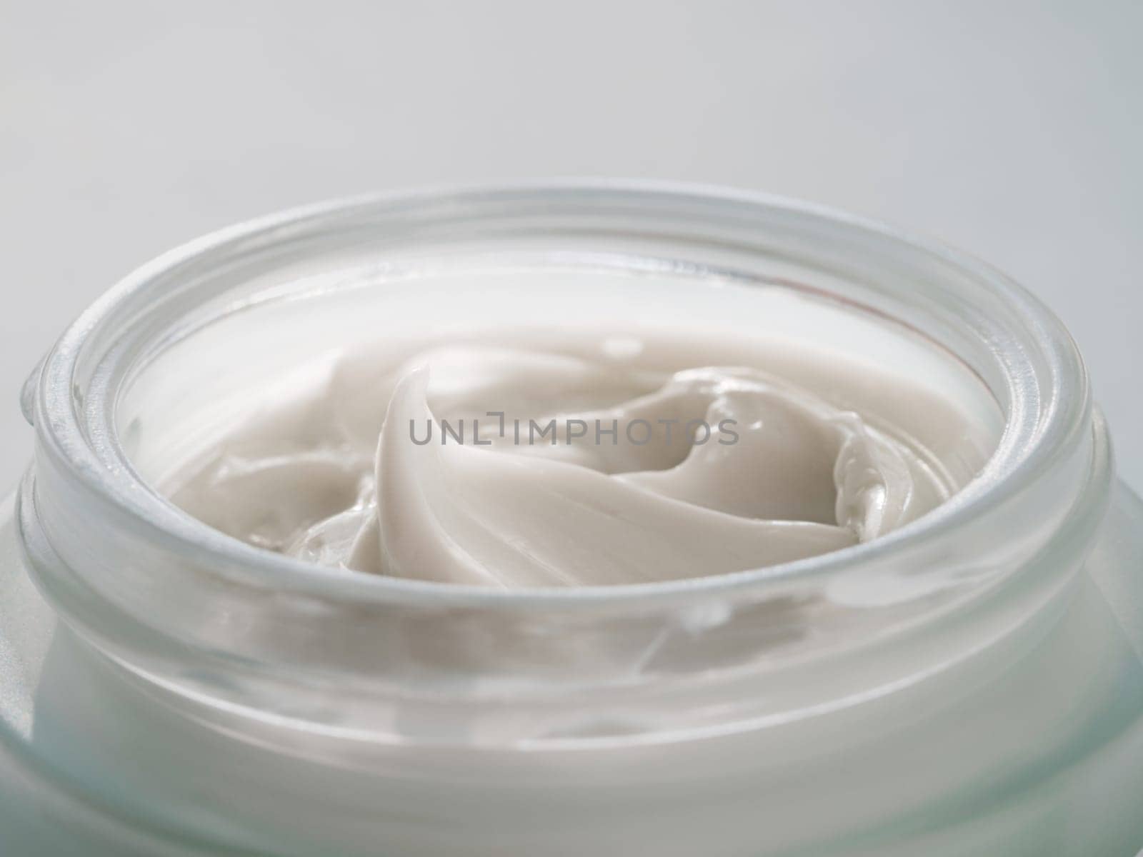 Glass jar of luxury face cream. Close up open jar with beautiful swirls of white cream in natural daylight. Texture of cosmetic cream in jar