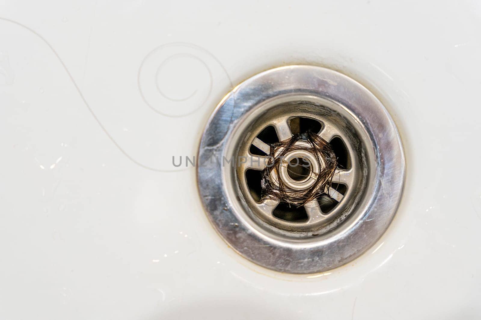 Close-up of long hair blocking the drain in the bathroom. Hair in the drain hole of the sink or shower. the problem of hair loss. To advertise shampoo. Clogging of the drain in the bathroom due to fallen hair.