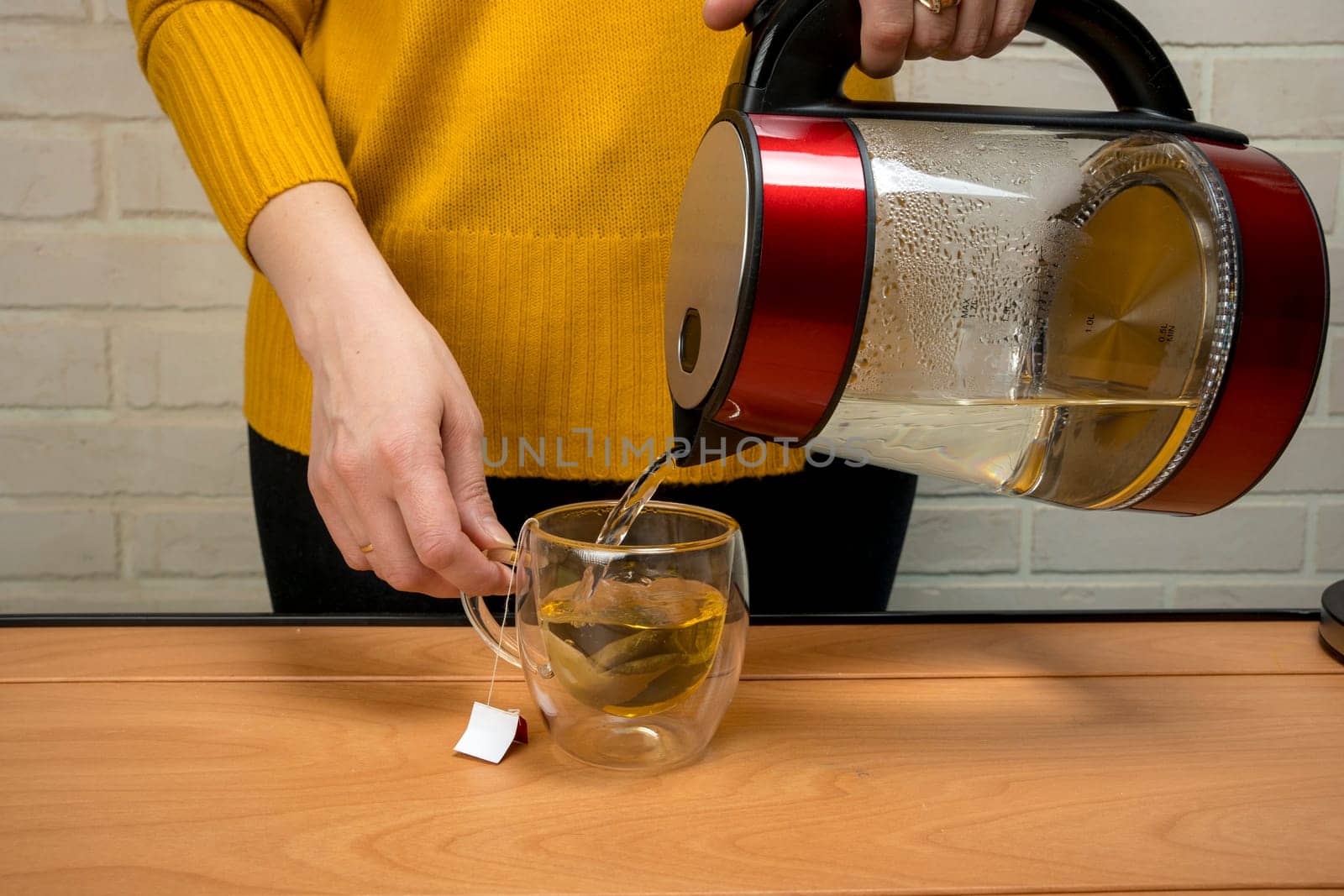 woman pouring hot water from a kettle into a clear glass mug by audiznam2609