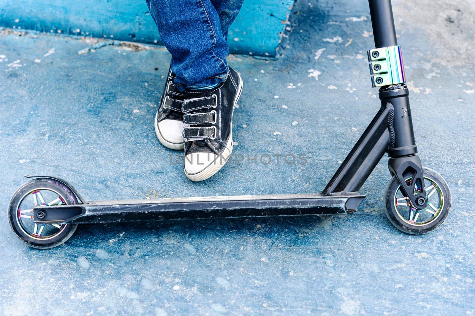 Rider boy legs close up in sneakers on stunt scooter on the skate park ramp. A boy on a scooter in a skate park performs jumps and tricks. extreme city sports outdoor Extreme jumping on a scooter. The concept of a healthy lifestyle. sports leisure