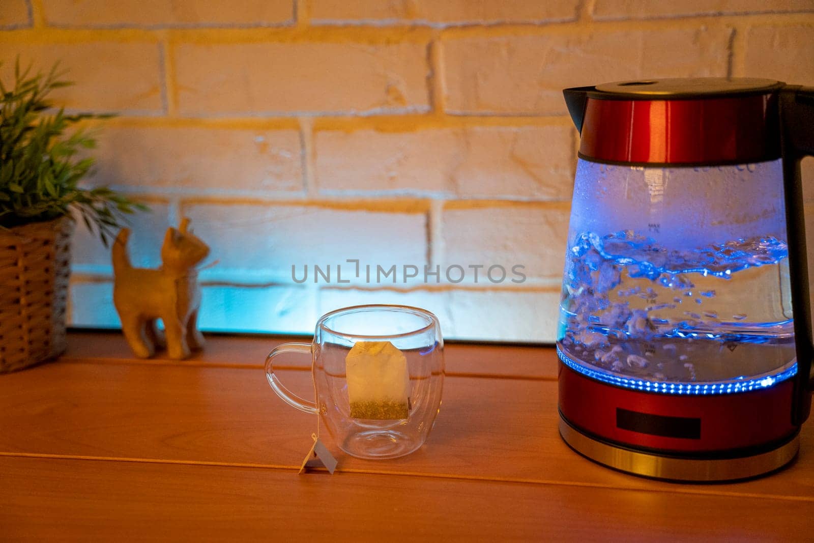 A glass electric kettle on a wooden table and a transparent mug with a bag of delicious tea. High quality photo