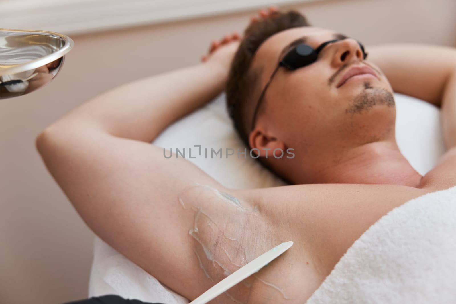 young man with protective goggles undergoes procedure of arm pit laser epilation in clinic