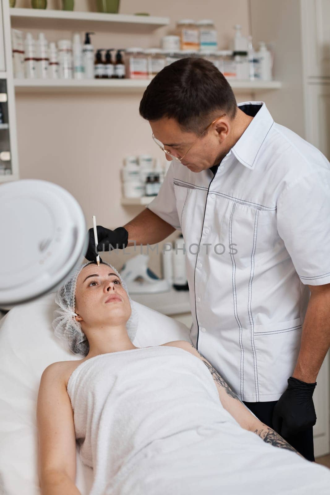 male cosmetologist marking skin of caucasian woman with white pencil. facial marking for aesthetic procedure.