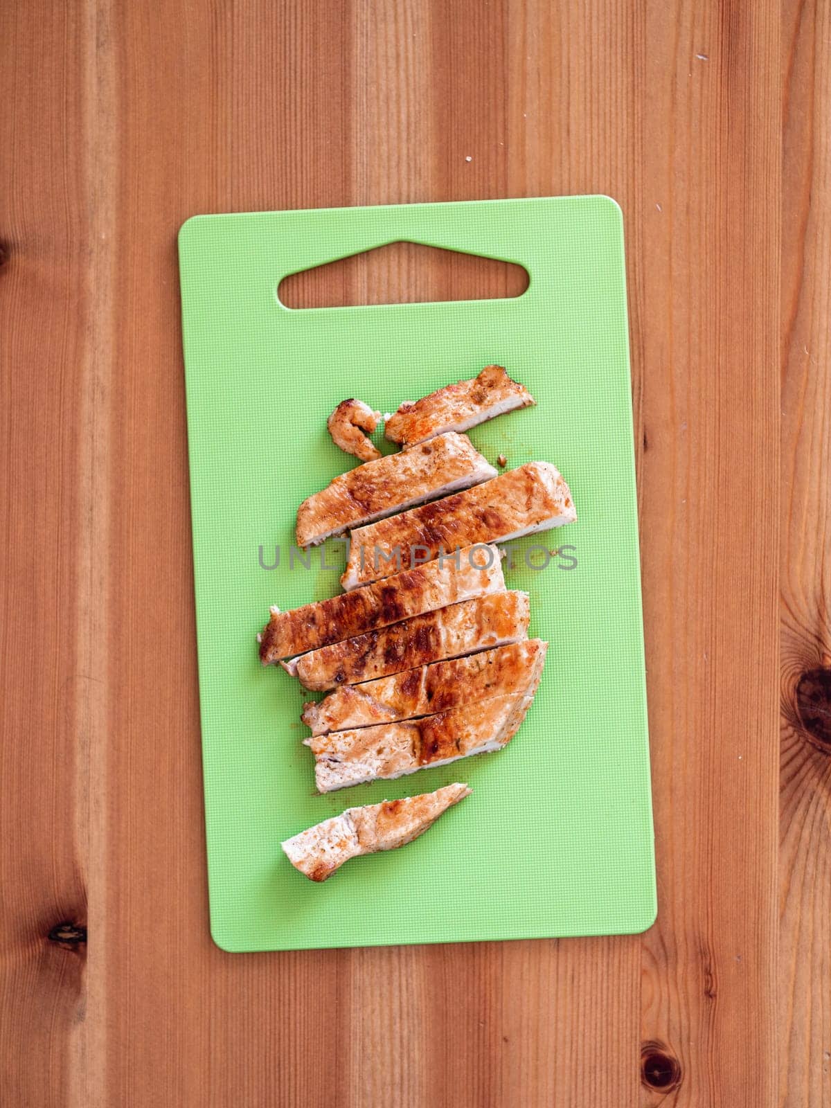 Grilled turkey meat steak sliced on cutting board over wooden tabletop. Perfect ready-to-eat turkey fillet on green cutting board top view or flat lay. Striped cooked fillet of turkey meat. Vertical