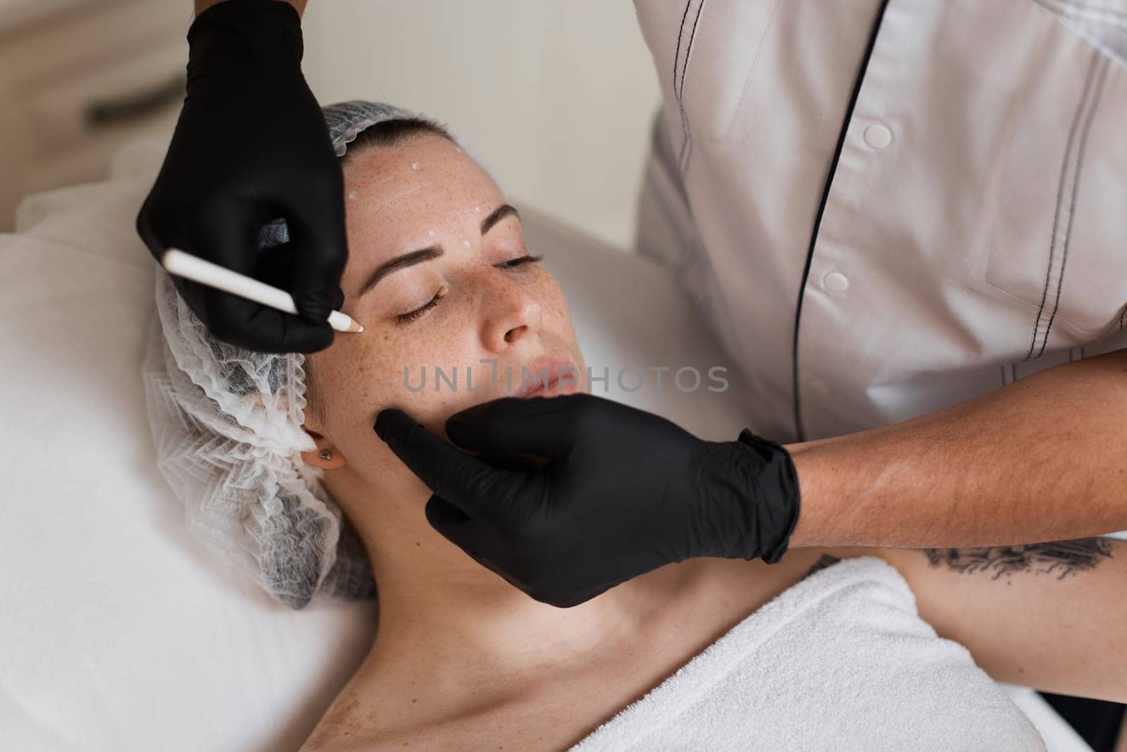 male cosmetologist marking skin of caucasian woman with white pencil. facial marking for aesthetic procedure.