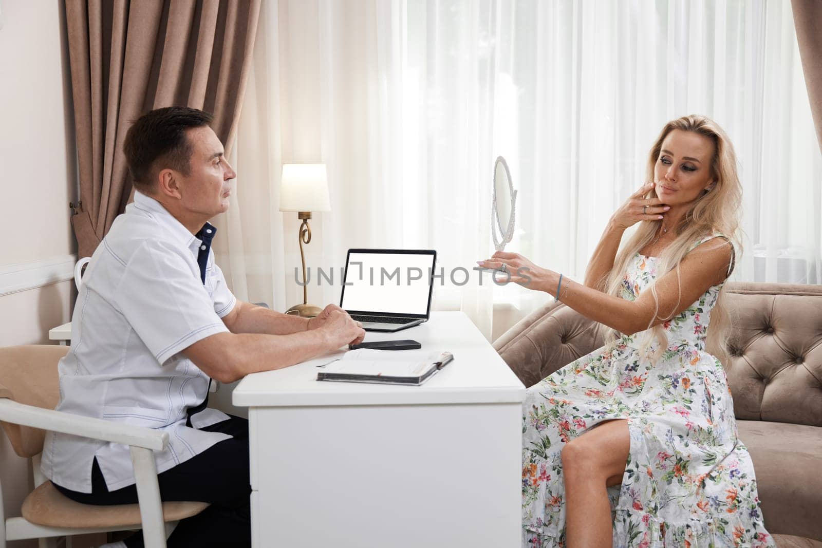 Beautiful blonde woman talking with male doctor about face aesthetic treatment in beauty medical clinic.