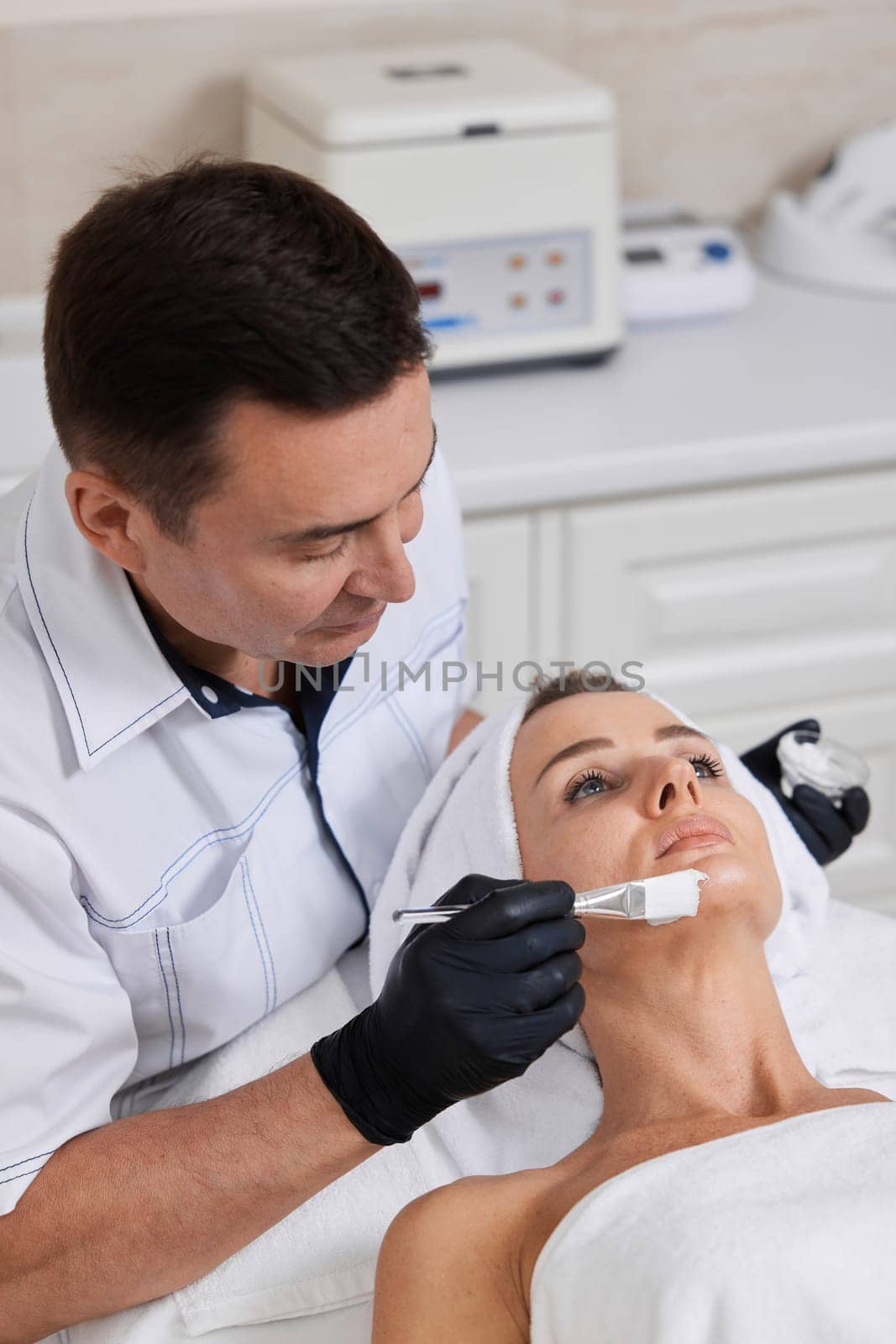 male beautician applies the mask to the face of beautiful woman in the spa salon. facial skin care concept.