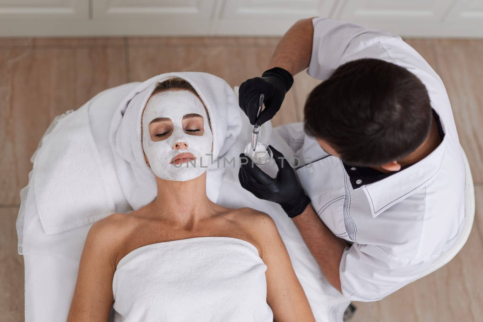 male beautician applies the mask to the face of beautiful woman in the spa salon. facial skin care concept.