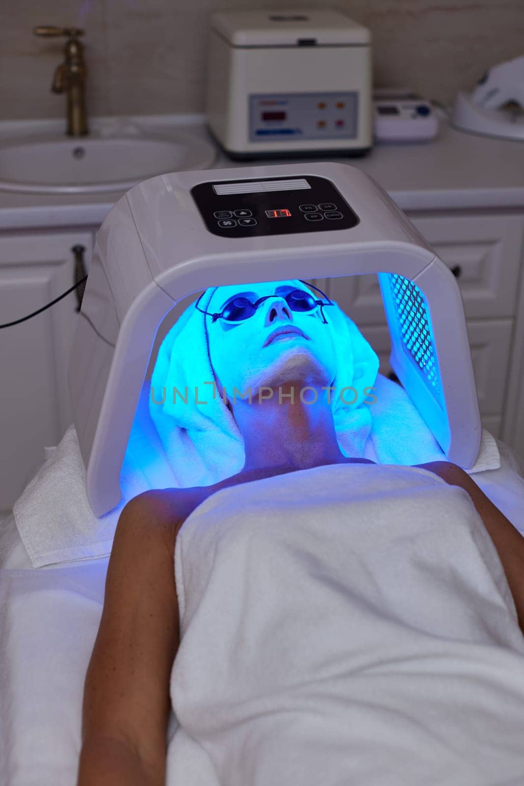 Woman in protective glasses getting facial treatment with led therapy. LED mask at the beauty clinic
