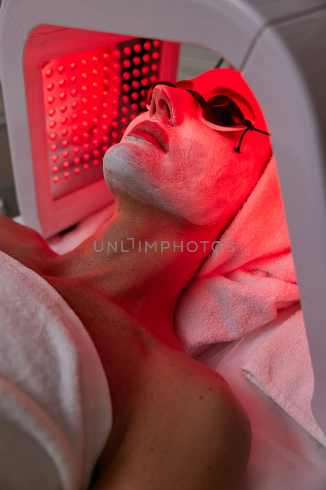 Woman in protective glasses getting facial treatment with led therapy. LED mask at the beauty clinic