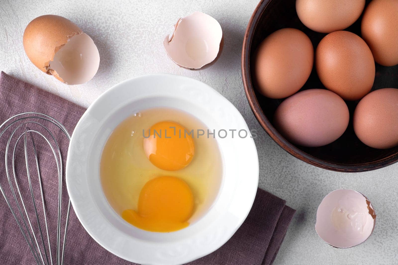 Top view brown chicken eggs in a bowl on the table with a whisk to beat the eggs.