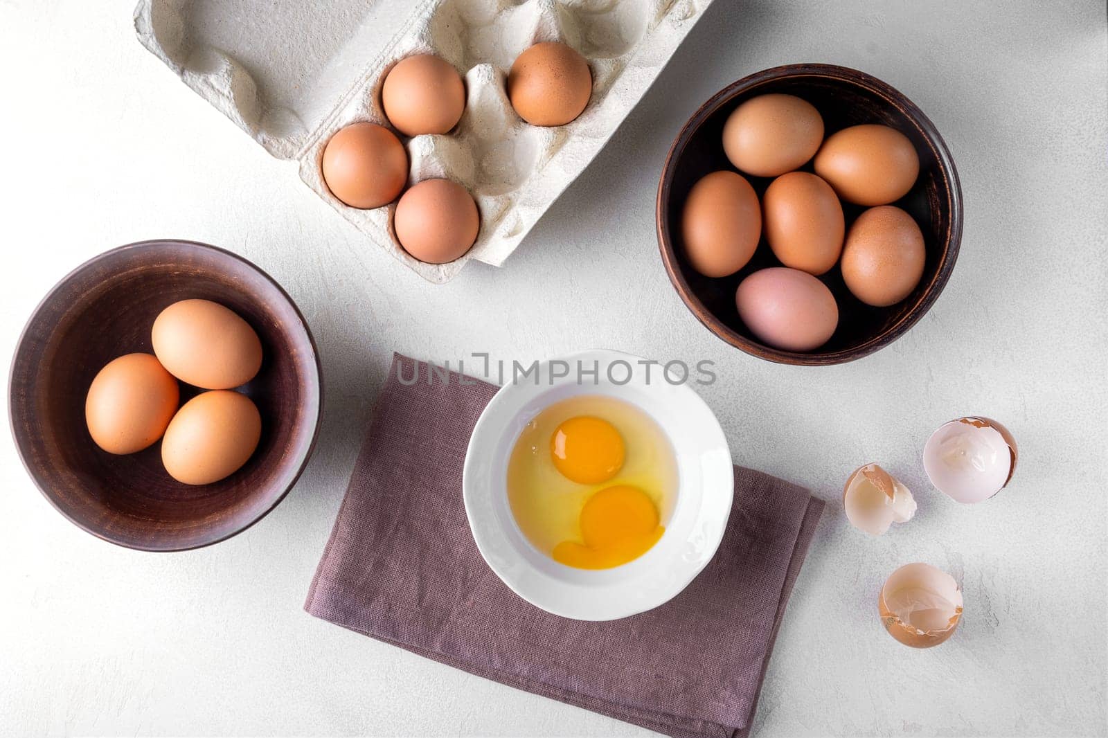 View from above brown chicken eggs in a cardboard packing container, and in a bowl on a table .