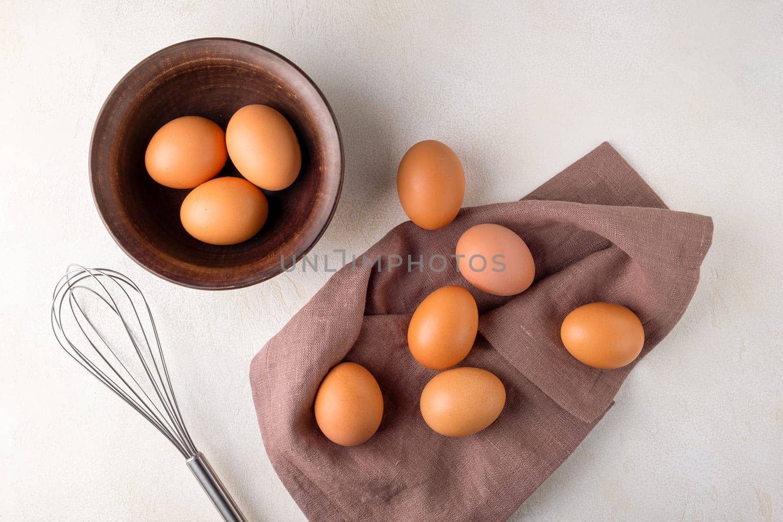 View from above brown chicken eggs in a bowl on a table with a whisk to beat the eggs.