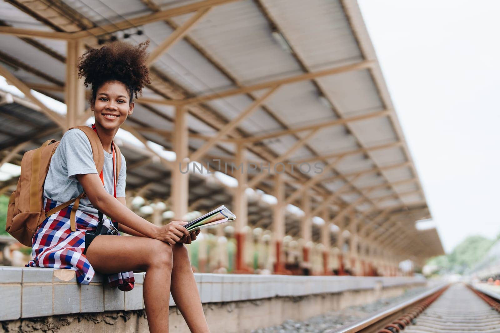 Asian teenage girl african american traveler dressed in casual wear holding map and searching right direction of route setting while waiting for a train at the station. by Manastrong