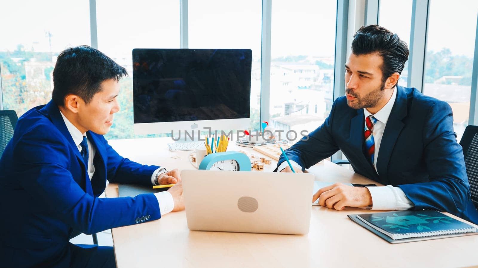 Two business people talk project strategy at office meeting room. Businessman discuss project planning with colleague at modern workplace while having conversation and advice on financial report. Jivy