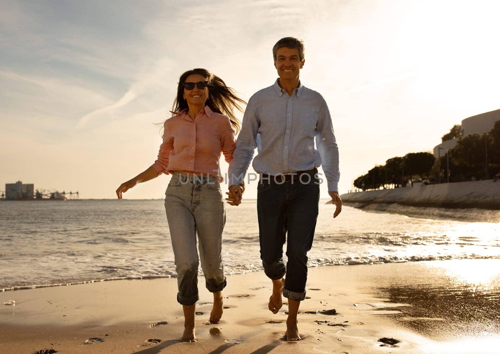Cheerful Middle Aged Couple Running On The Beach In Summer Time, Happy Mature Man And Woman Holding Hands And Smiling, Husband And Wife Having Fun Together During Date Outdoors, Copy Space