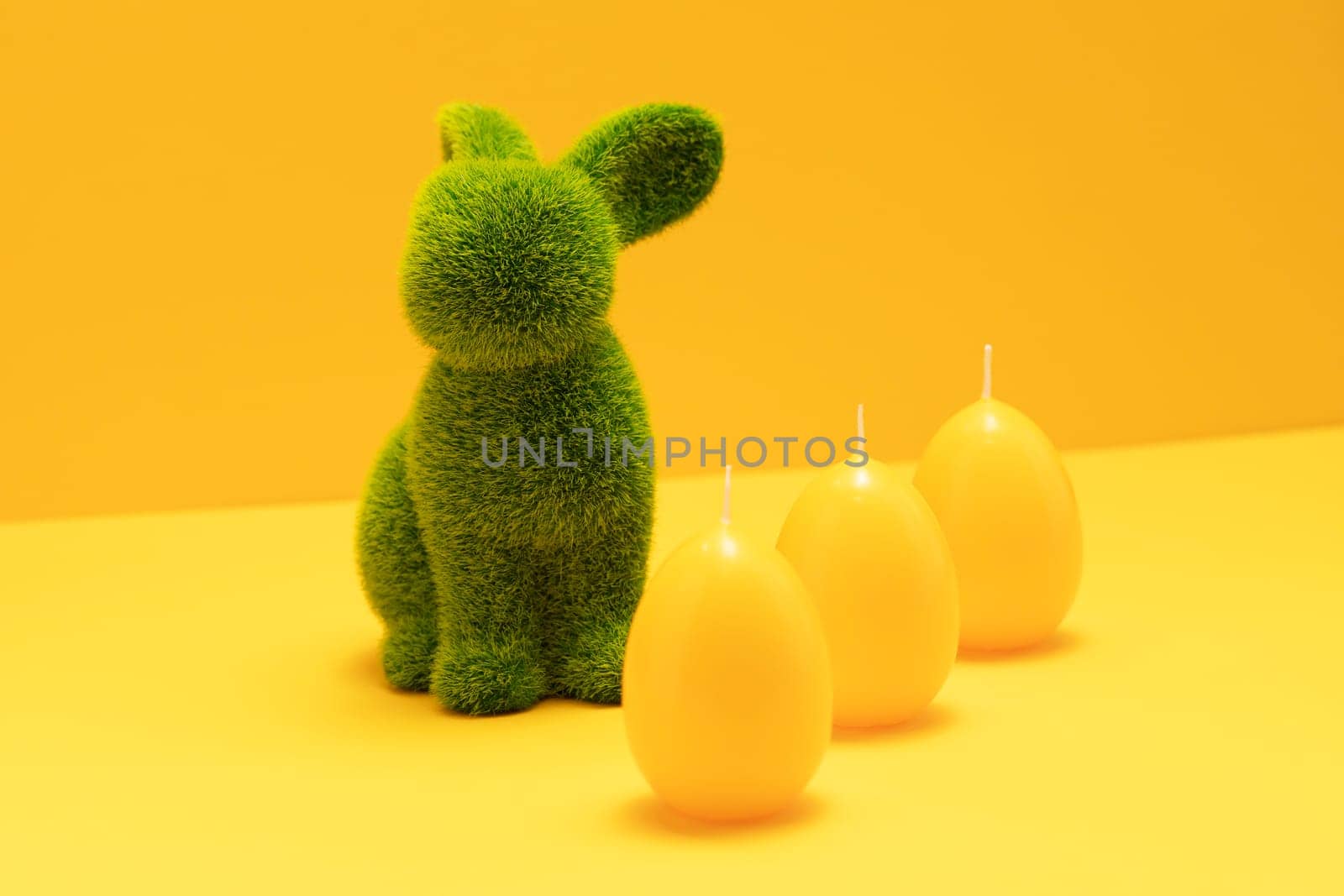Green Easter Bunny with three yellow candles of eggs shape on matching monochrome orange background. Minimal Happy Easter holiday concept. Creative festive Easter greeting card, copy space for text
