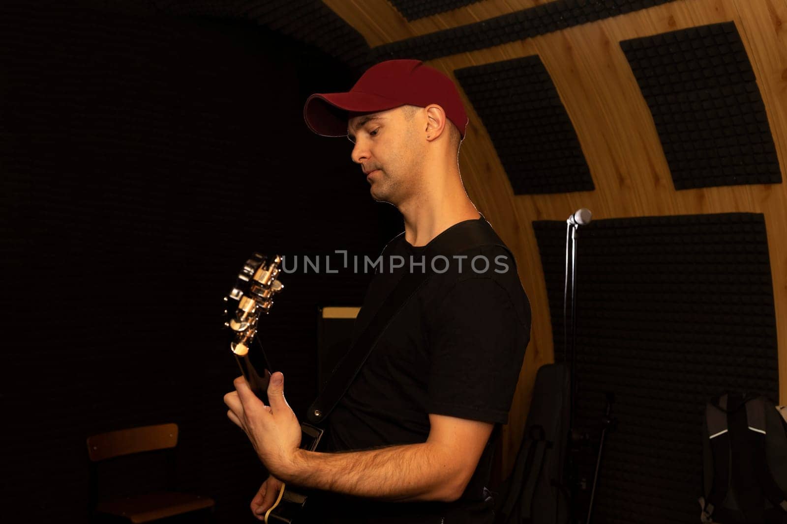 Caucasian man plays guitar, holding musical instrument in hands, standing in studio. Darken photo. Male wears casual cloth. Hobby, leisure of creative person, artist. Copy space. Horizontal