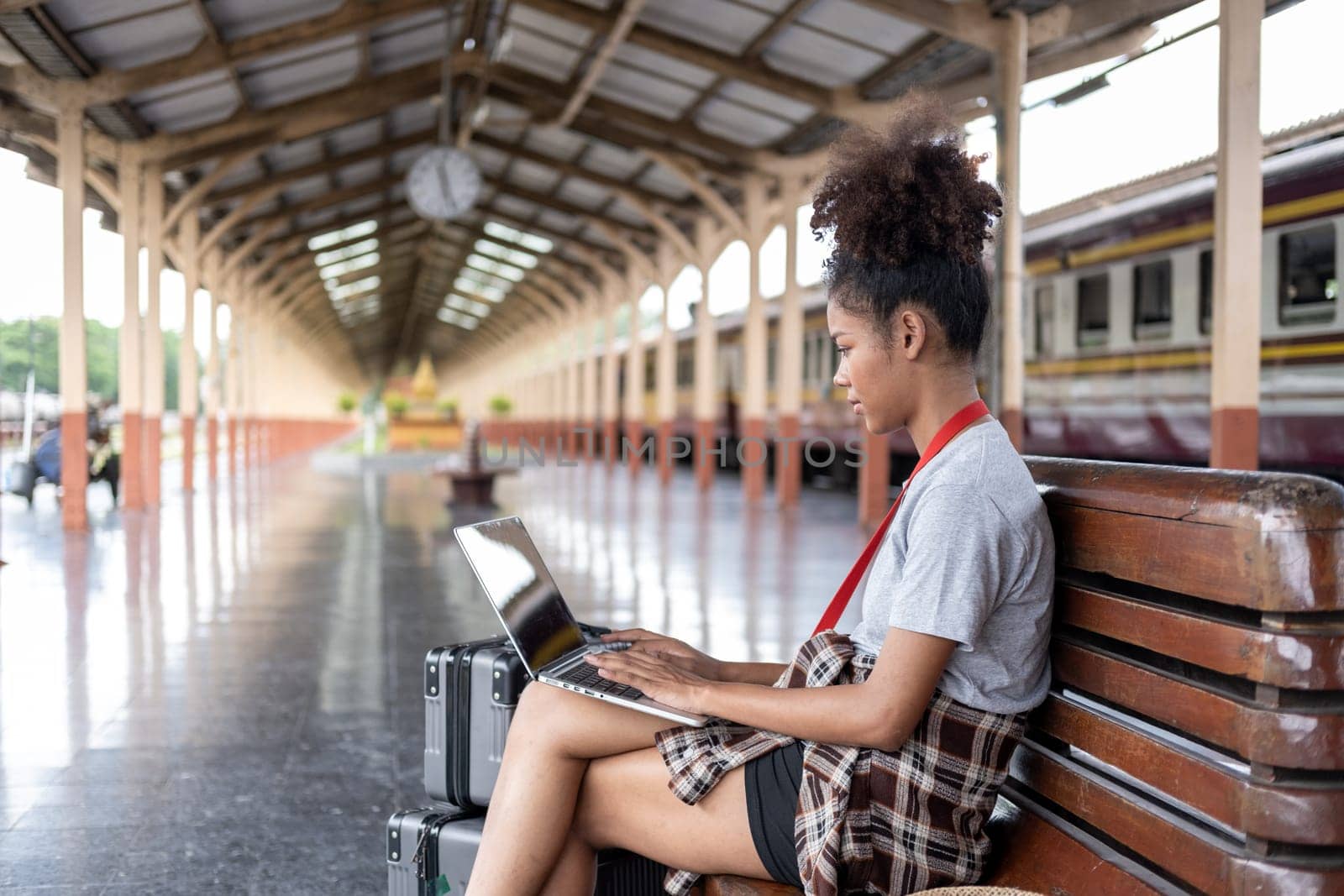 Young woman girl female sitting use computer laptop and travel bag suit case on the floor at station by wuttichaicci