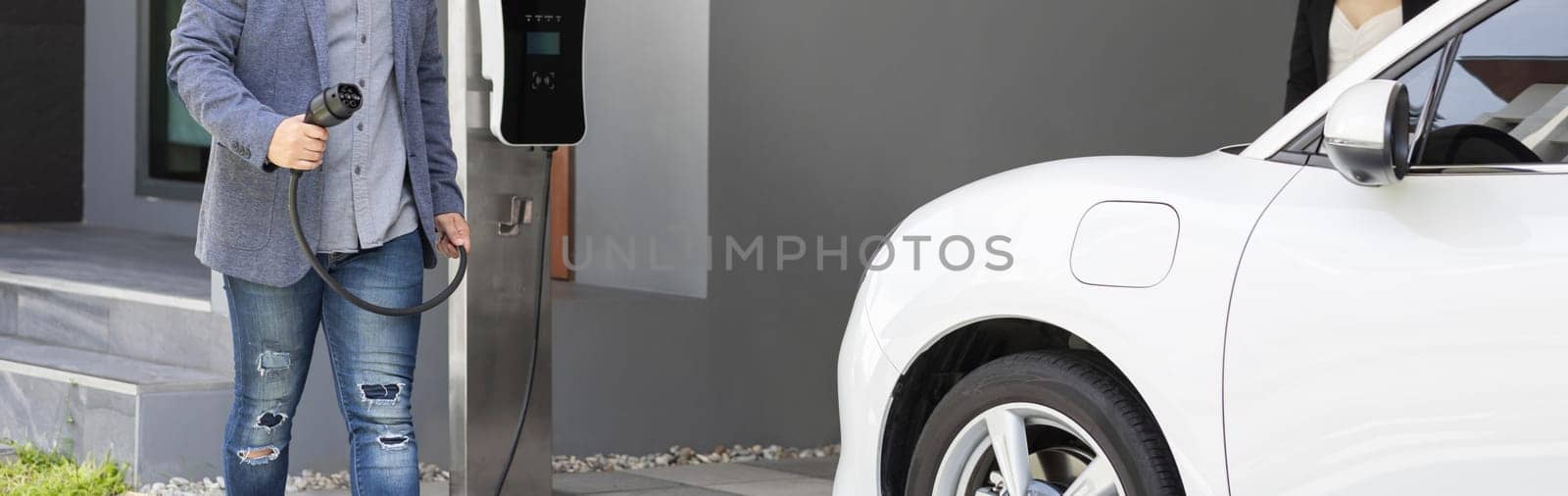 Closeup progressive asian man recharge his EV car at home charging station. by biancoblue