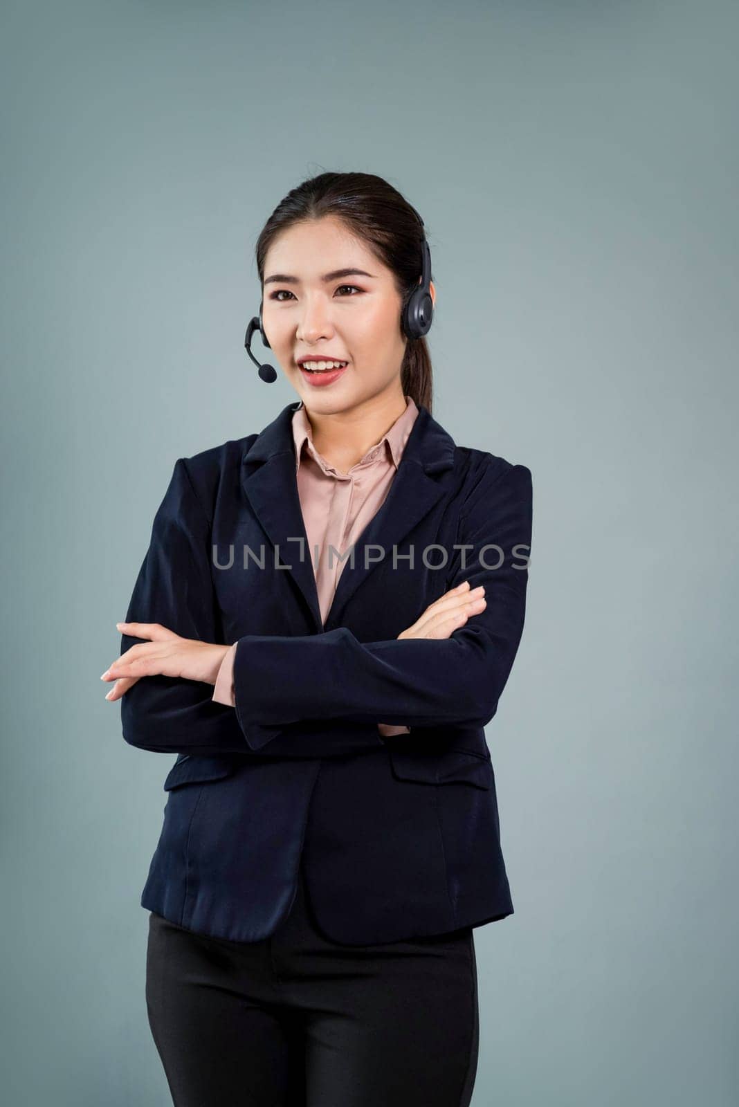 Attractive asian female call center operator with happy smile face advertises job opportunity on empty space, wearing a formal suit and headset on customizable isolated background. Enthusiastic