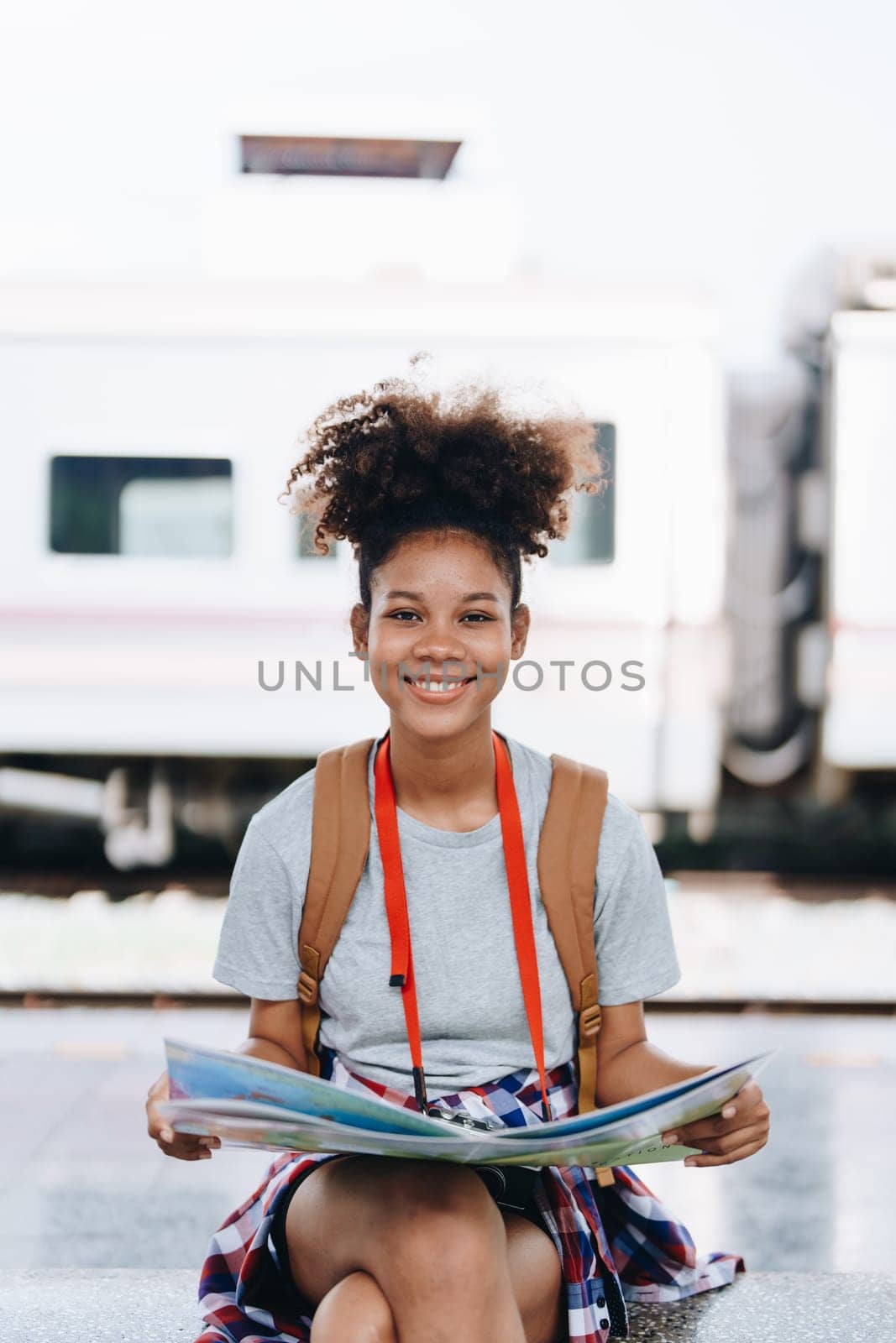 Asian teenage girl african american traveler dressed in casual wear holding map and searching right direction of route setting while waiting for a train at the station. by Manastrong