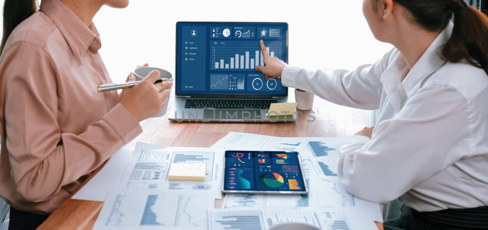 Analyst team colleague discuss financial data on digital dashboard, analyzing charts graph display on laptop and tablet screen. Modern office use business intelligence to plan marketing. Enthusiastic