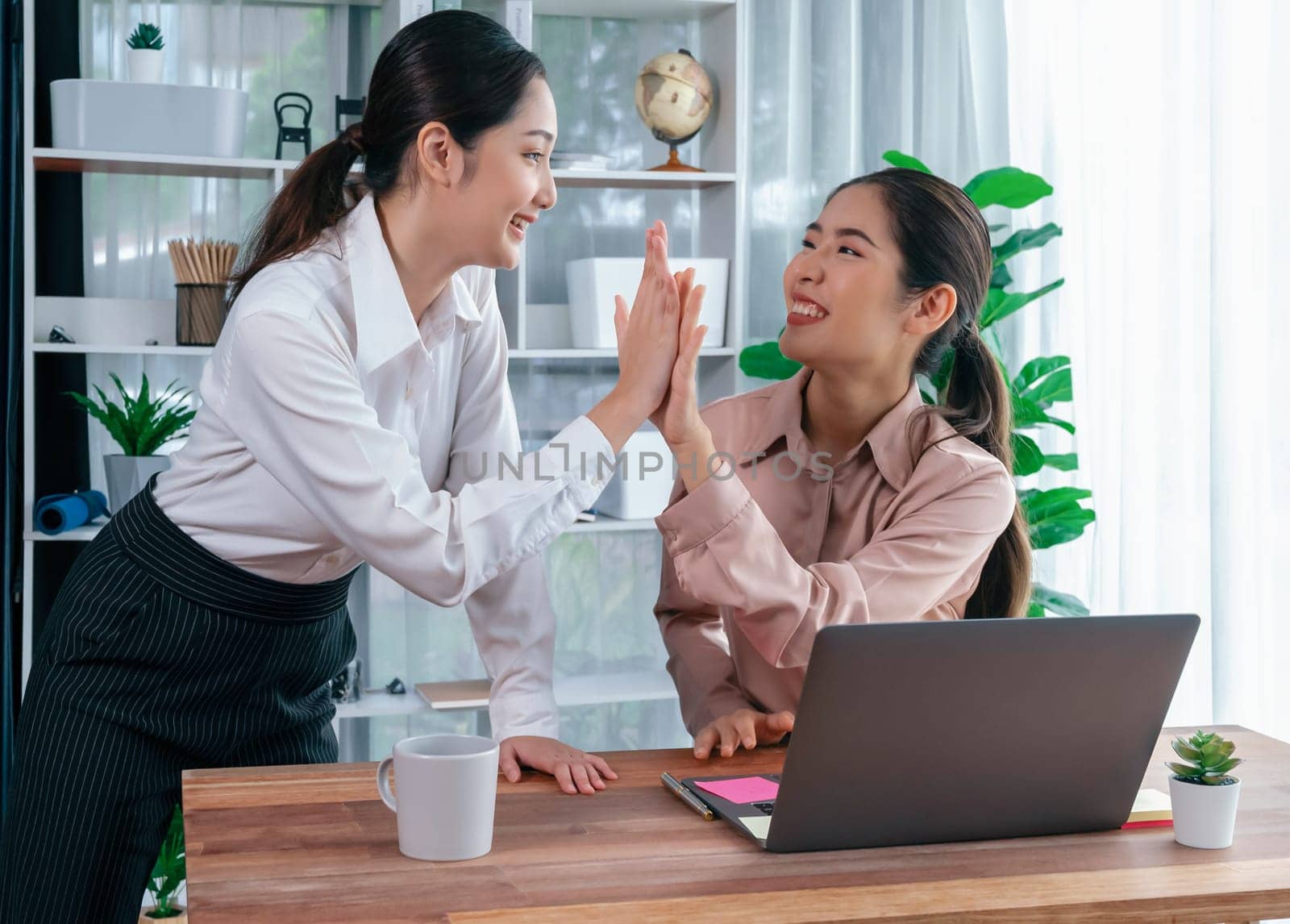 Colleagues in the office workspace give high-five to celebrate completing a project or finding a solution to a problem, showcasing a strong sense of teamwork and friendship in workplace. Enthusiastic