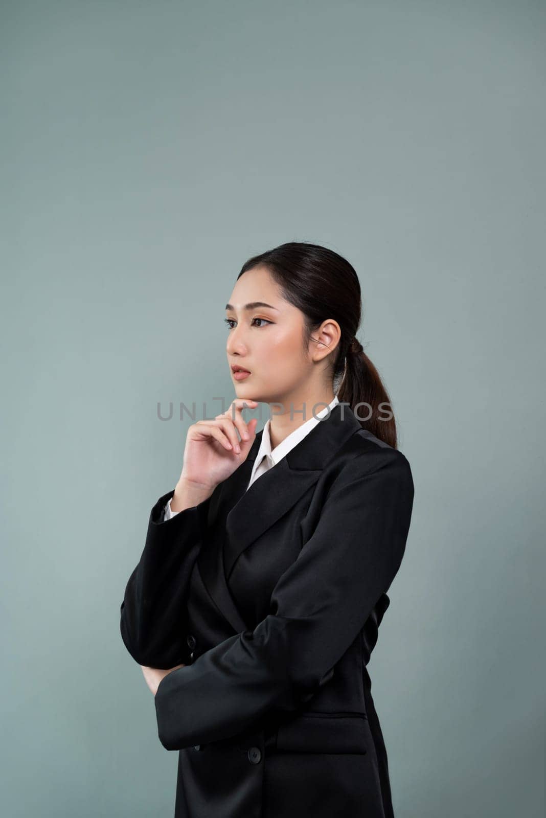 Confident young businesswoman stands on isolated background, posing in formal black suit. Office lady or manager with smart and professional appearance. Enthusiastic