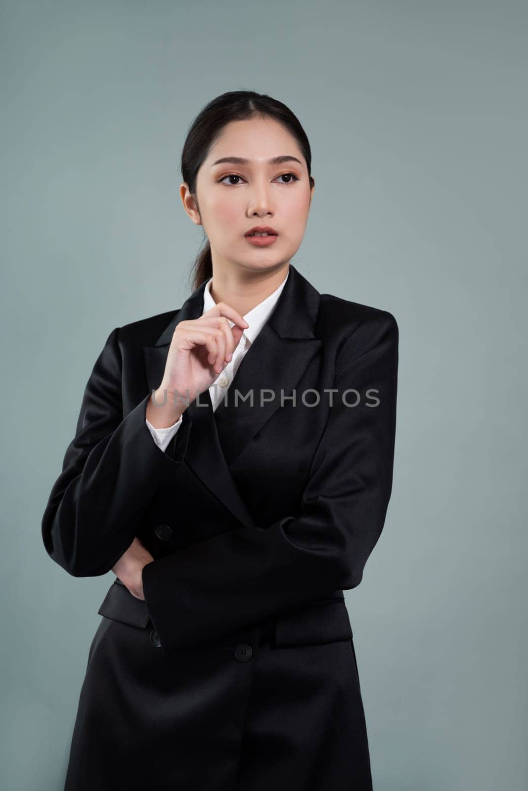 Confident young businesswoman stands on isolated background, posing in formal black suit. Office lady or manager with smart and professional appearance. Enthusiastic