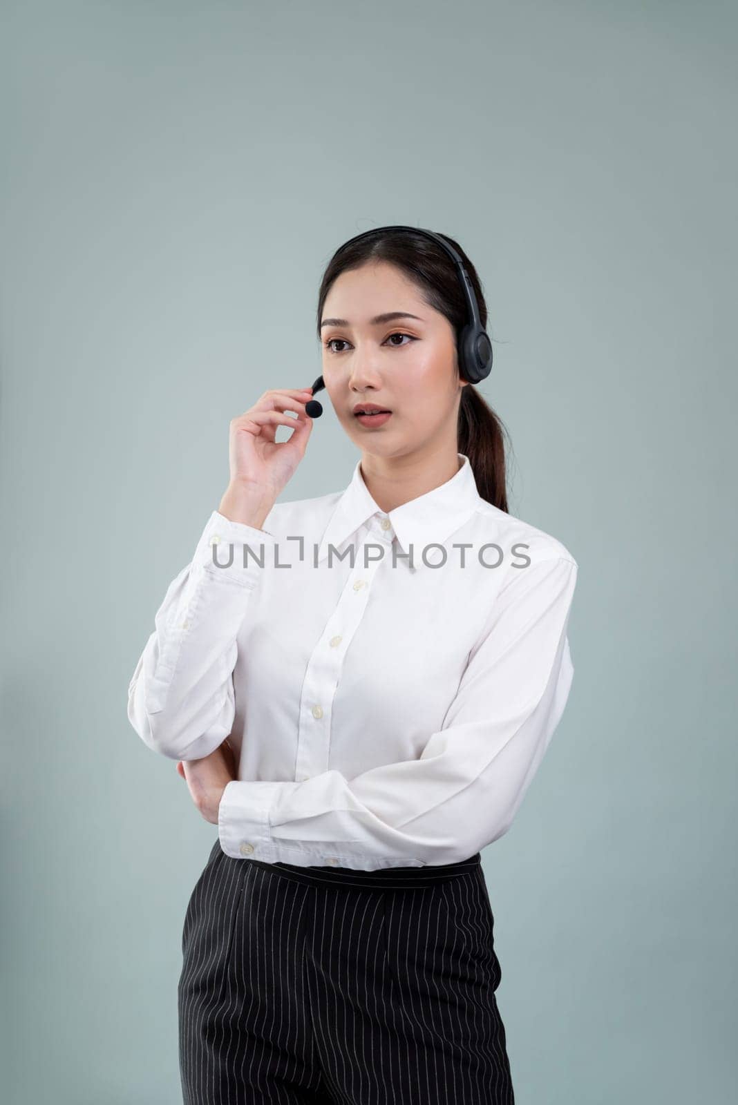 Attractive asian female call center operator with happy smile face advertises job opportunity on empty space, wearing a formal suit and headset on customizable isolated background. Enthusiastic