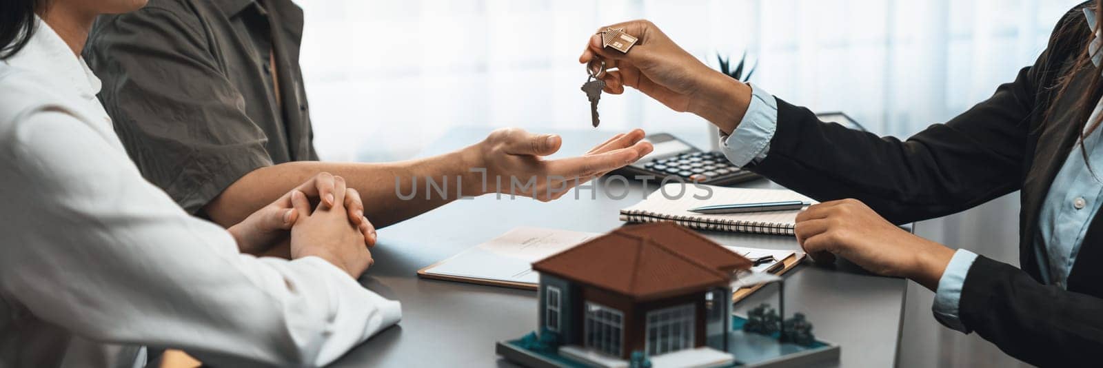 Real estate agent hand over house key to buyer after successful payment on house loan. Ownership transfer and deal completion in housing business concept in panorama view with house model. Prodigy