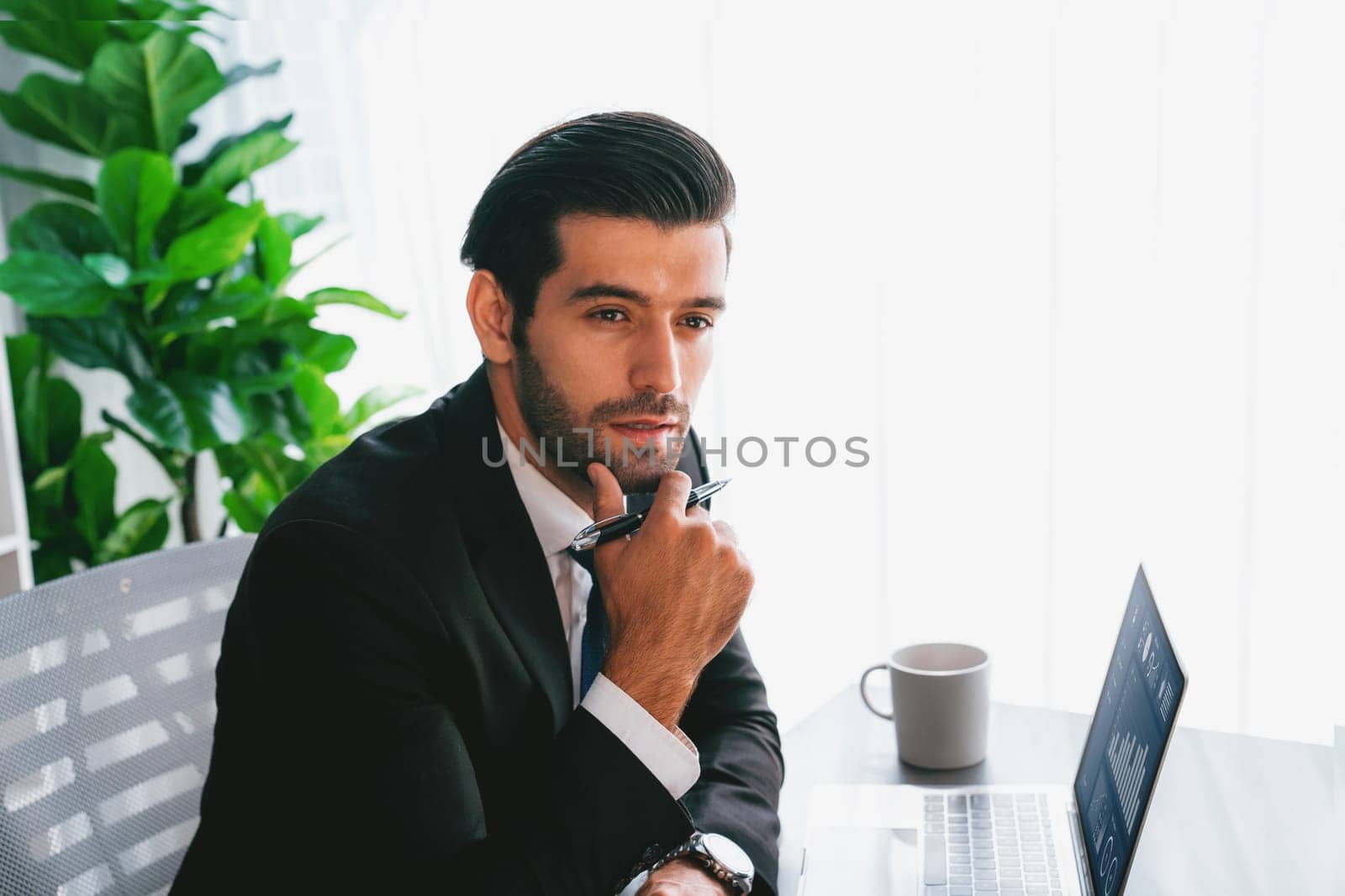 Modern professional businessman at modern office desk using laptop to work and write notes. Diligent office worker working on computer notebook in his office work space. fervent