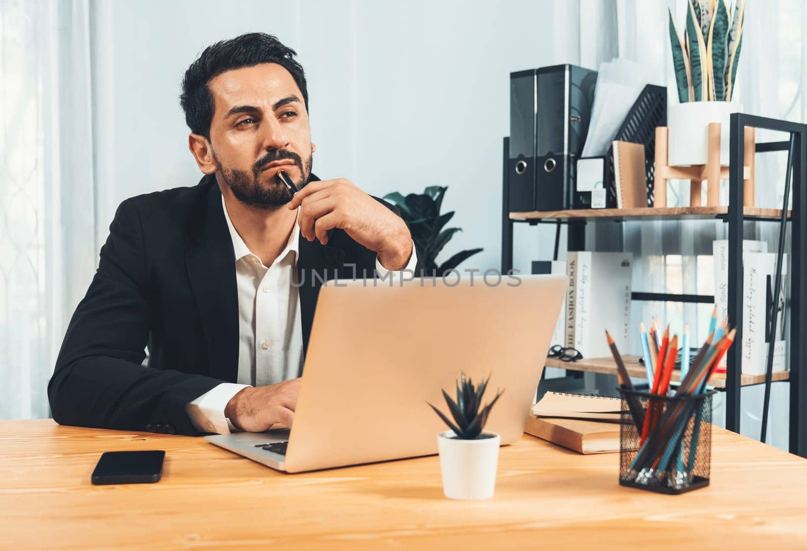 Modern professional businessman at modern office desk using laptop to work and write notes. Diligent office worker working on computer notebook in his office work space. fervent