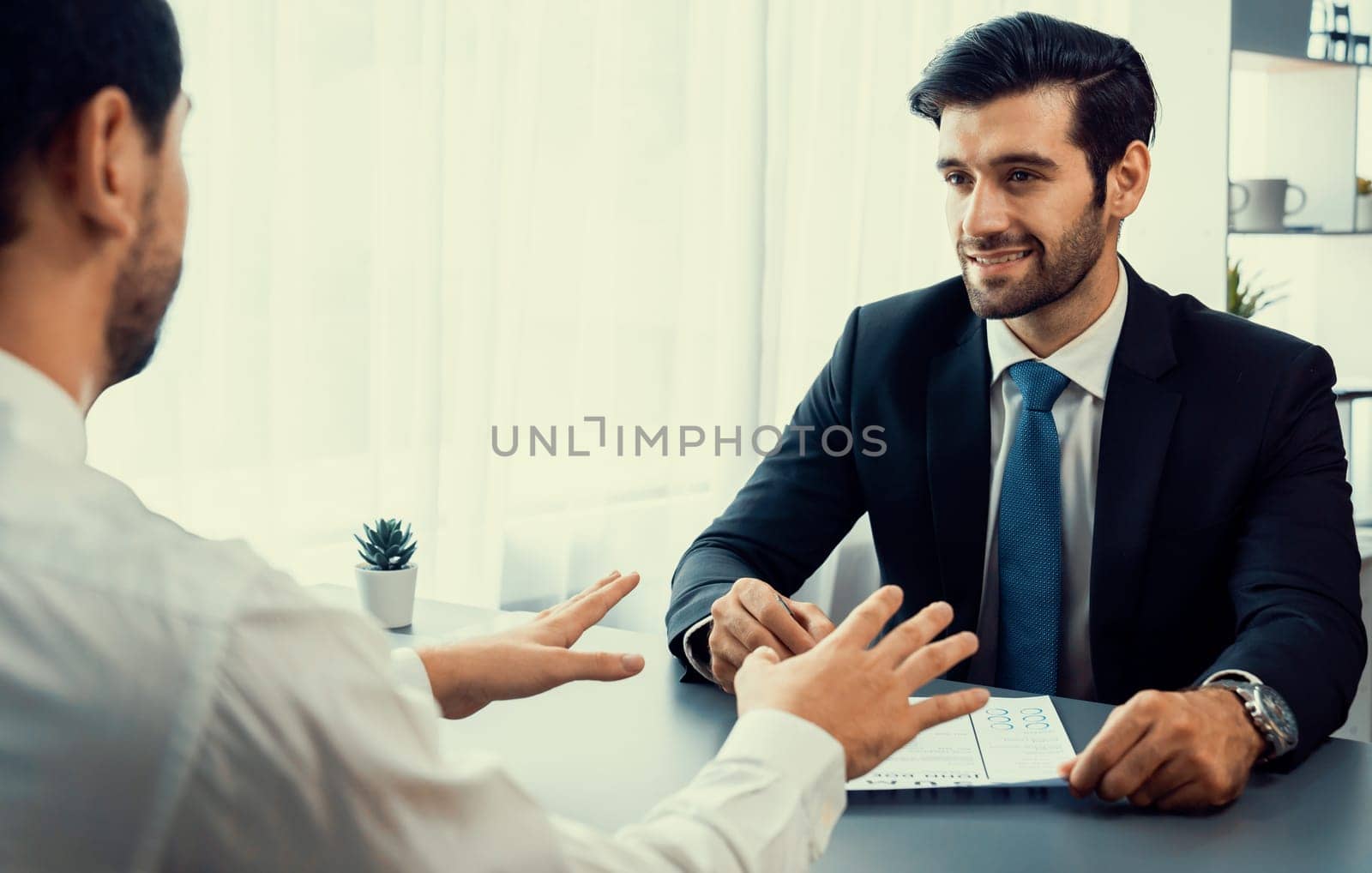 Interviewing job applicant in office with resume paper. Candidate wear suit for formal conversation with interviewer. Recruitment process with question about career and work experience. Fervent