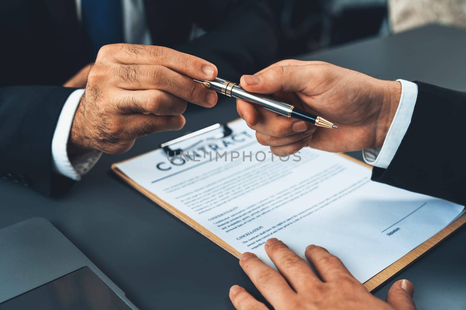 Two businesspeople sit across the desk as business deal is taking place. Corporate attorney giving a pen for client or partner to sign contract paper, sealing the deal with signature. Fervent